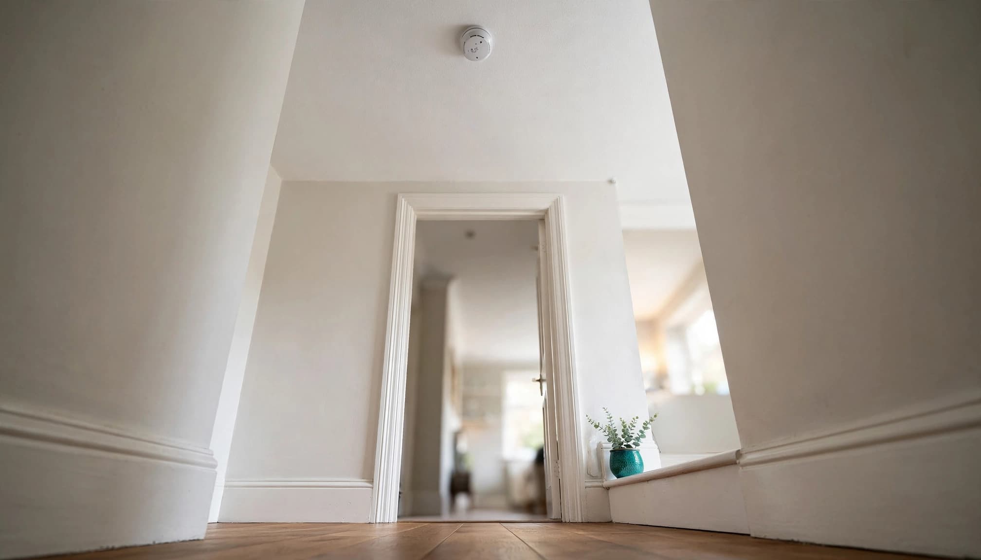 A smoke alarm mounted on a white hallway ceiling above a doorway.